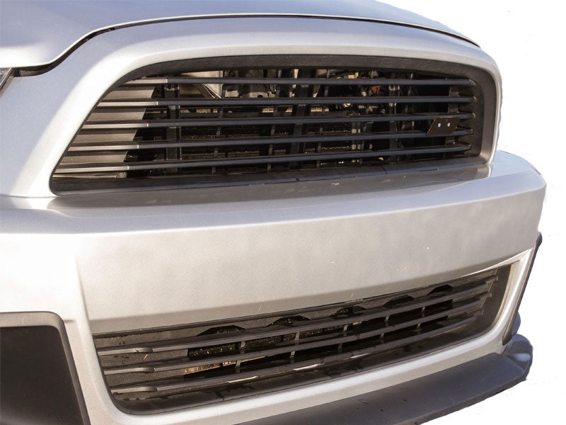 
                  
                    Close-up of the front grille and bumper of a silver 2013-2014 Ford Mustang, featuring two black horizontal injection-molded TPO grilles and part of the car’s headlight on the left.
                  
                