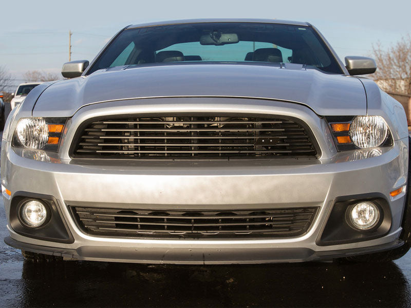 
                  
                    Front view of a silver 2013-2014 Ford Mustang parked outdoors, featuring its grille, headlights, and bumper with a Roush Lower Grille Kit made from injection-molded TPO.
                  
                