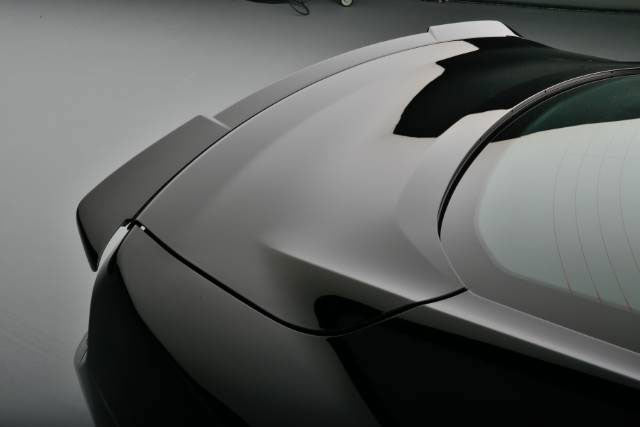 
                  
                    Close-up of a sleek black Mustang's rear, featuring curved lines and a tinted window, accentuated by a Mustang rear spoiler, set against a gray background.
                  
                