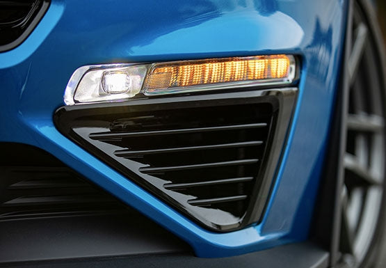 
                  
                    Close-up of a car's front bumper showing an illuminated daytime running light and amber turn signal on a blue vehicle equipped with the ROUSH Stage 3 Max Cooling Upgrade.
                  
                