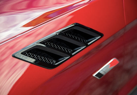 
                  
                    Close-up of a black side vent and a metallic ROUSH Stage 3 badge on the red exterior of a car, highlighting the enhanced Mustang cooling system.
                  
                