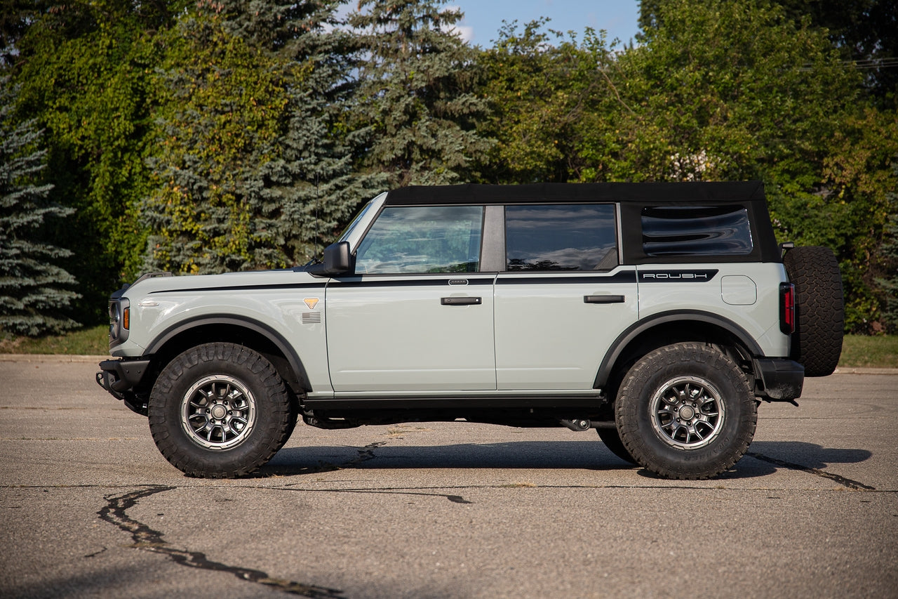 
                  
                    A light green Ford Bronco parked on an asphalt road, featuring 2021-2024 Roush Bronco & Ranger 17-inch Iridium Grey wheels and a spare tire on the rear by Roush Performance Products, Inc.
                  
                