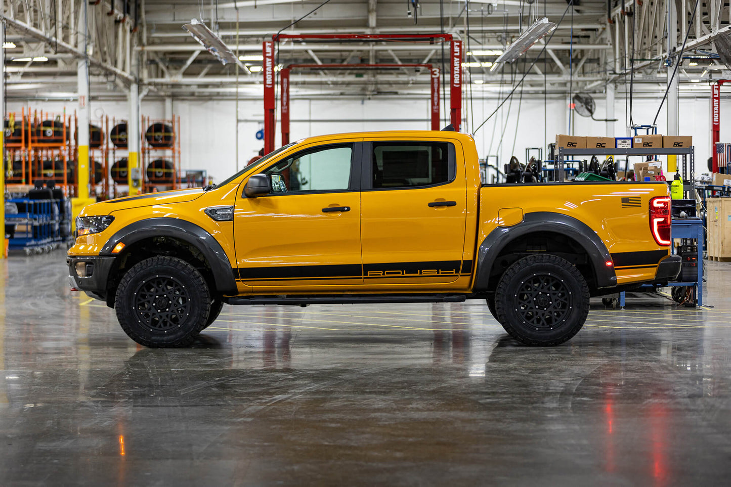 
                  
                    A yellow 2022 Roush Ranger pickup truck, known for its off-road capability, is parked inside an industrial garage, with equipment and machinery visible in the background. The truck features black wheels and decals along the sides.
                  
                