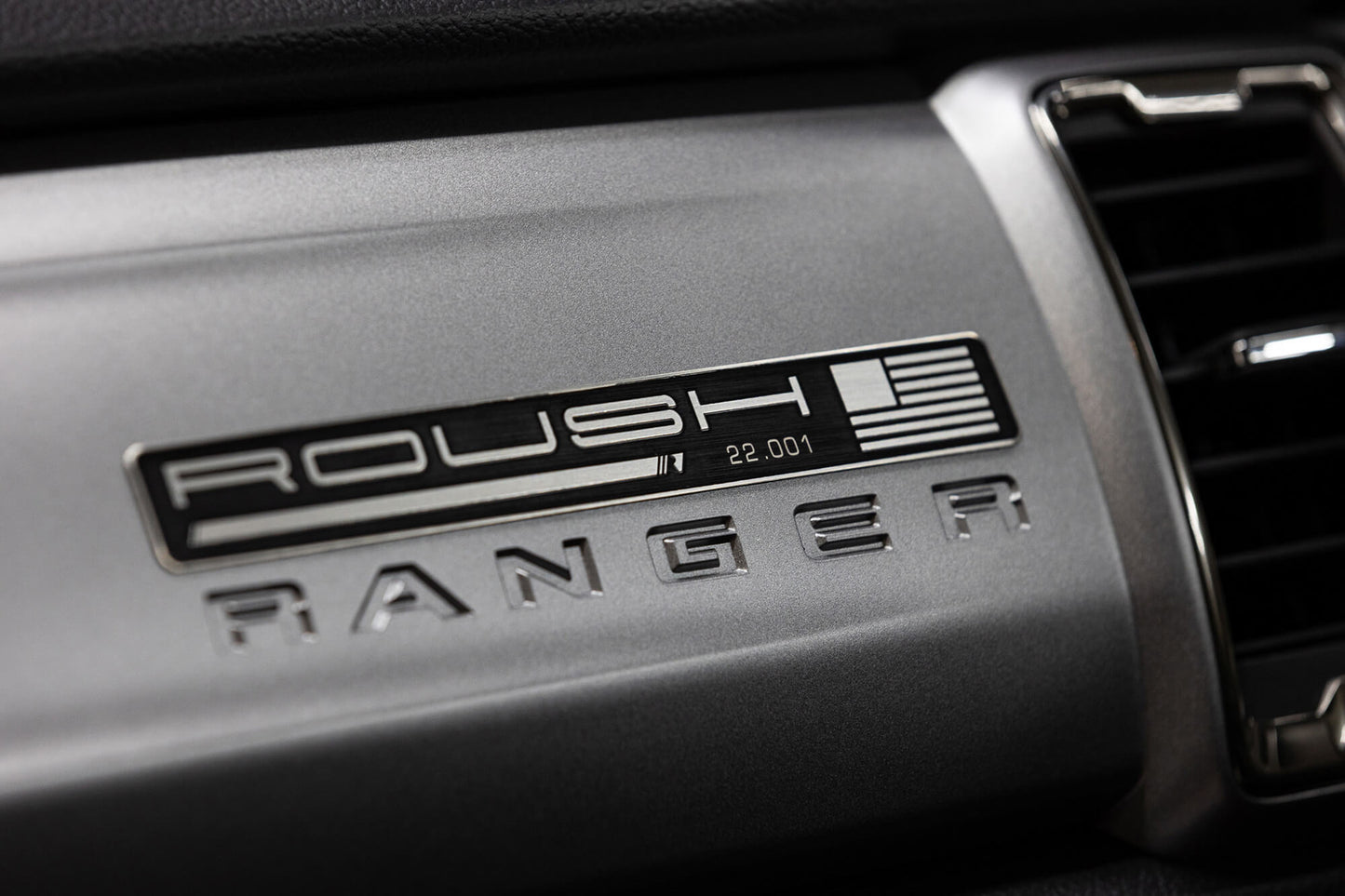 
                  
                    Close-up of a 2022 Roush Ranger's dashboard showcasing the Roush Ranger badge and the serial number 22-001, positioned next to an air vent.
                  
                
