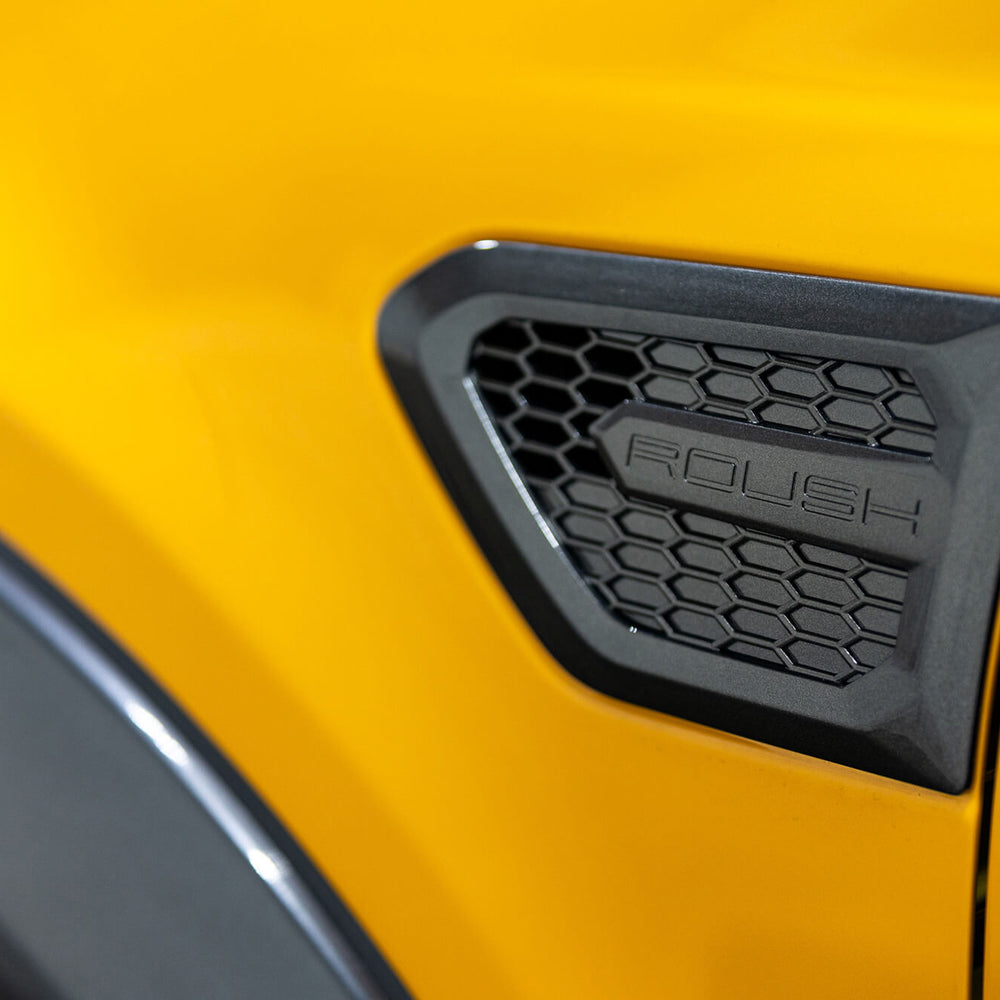 
                  
                    Close-up of a yellow 2022 Roush Ranger with a black, hexagon-patterned vent labeled "ROUSH" on the side, showcasing its off-road capability.
                  
                