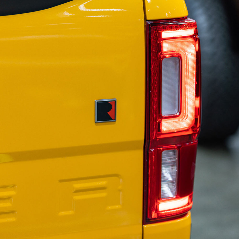 
                  
                    Close-up of the rear side of a yellow vehicle, showing a distinct red and black emblem near the tail light, emphasizing the 2022 Roush Ranger's off-road capability.
                  
                