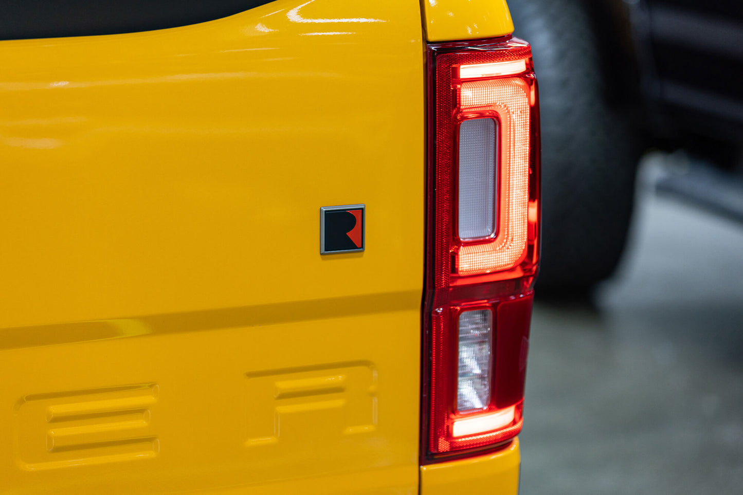 
                  
                    Close-up of the rear side of a yellow vehicle, showing a distinct red and black emblem near the tail light, emphasizing the 2022 Roush Ranger's off-road capability.
                  
                
