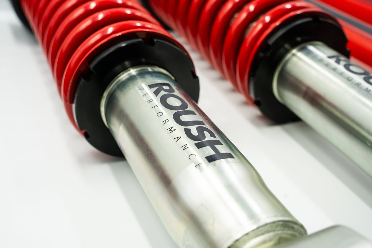 
                  
                    Close-up of a Roush Performance automotive shock absorber with red coil spring, showing the brand name on the metal cylinder—part of a premium Roush Ram 1500 suspension performance system.
                  
                