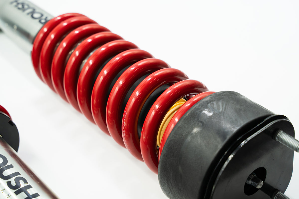 
                  
                    Close-up of a red coil spring and shock absorber assembly from a performance suspension system, designed for upgrades such as the Ram 1500 lift kit, set against a white background.
                  
                