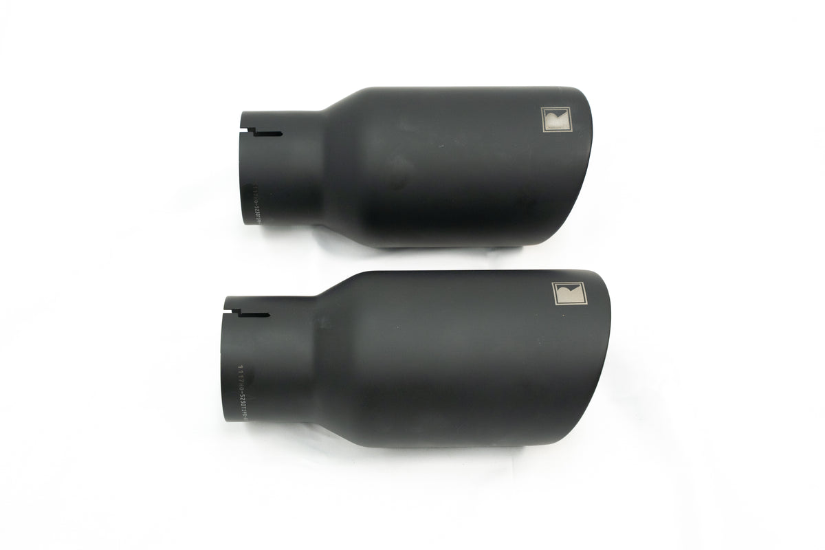 
                  
                    Two matte black cylindrical exhaust tips with angled ends and a small square logo on each, designed to complement a rear-exit exhaust system, shown on a white background.
                  
                