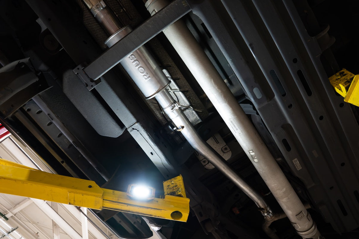 
                  
                    Underside of a Ram 1500 5.7L HEMI showing a Roush performance exhaust system and a yellow hydraulic lift arm.
                  
                