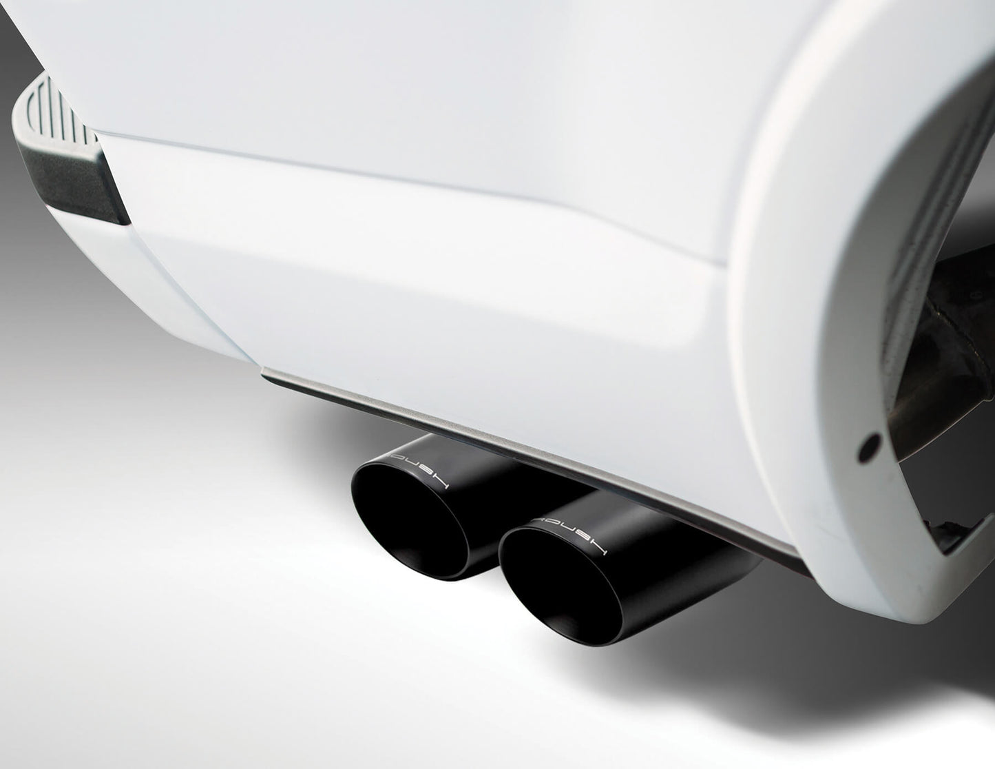 
                  
                    Close-up view of a car's dual black exhaust pipes extending from a white vehicle, showcasing the power and precision of a cat-back exhaust system.
                  
                