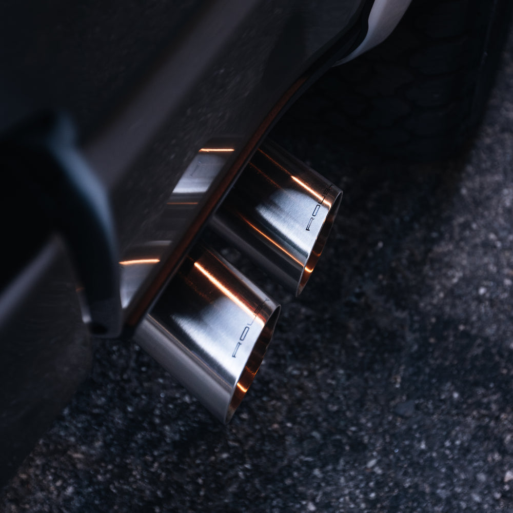 
                  
                    Close-up of dual chrome exhaust pipes on a dark-colored 2023 Roush F-150, parked on a paved surface, showcasing the power and style of Roush performance enhancements.
                  
                