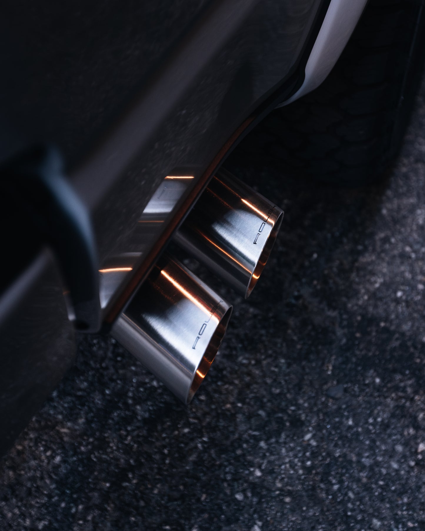 
                  
                    Close-up of dual chrome exhaust pipes on a dark-colored 2023 Roush F-150, parked on a paved surface, showcasing the power and style of Roush performance enhancements.
                  
                