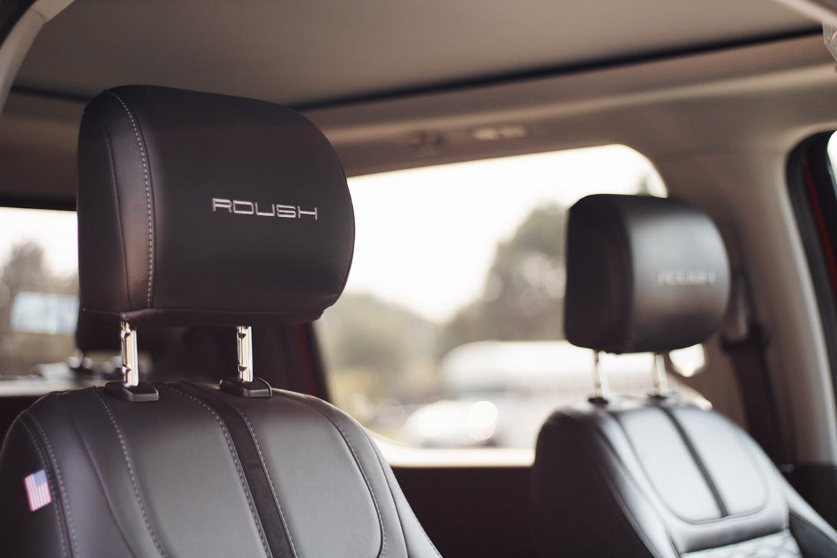 
                  
                    Interior view of a 2025 Roush Super Duty featuring dark leather headrests embroidered with the Roush logo.
                  
                