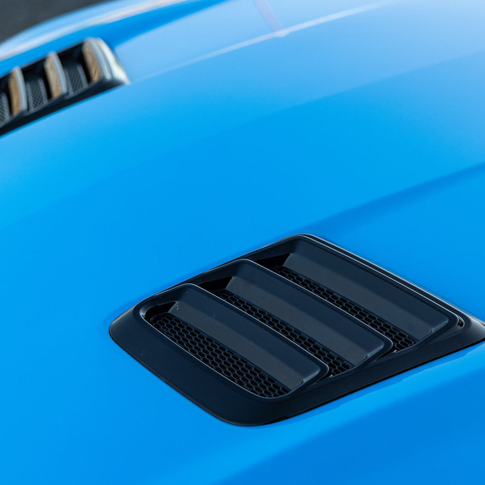 
                  
                    Close-up of a blue car hood featuring two Gloss Black Mustang Hood Heat Extractors with a three-slot design, showcasing Roush Performance.
                  
                