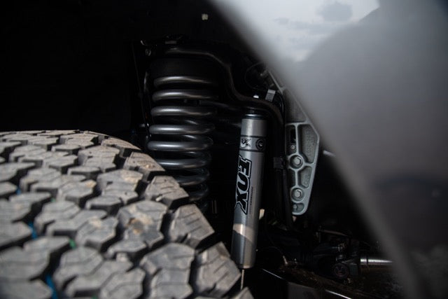 
                  
                    Close-up of a 2023 Roush Super Duty’s performance suspension system showing a coiled spring, a Fox shock absorber, and part of a large all-terrain tire.
                  
                