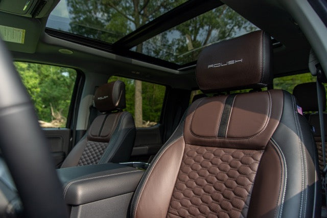 
                  
                    View of a 2023 Roush Super Duty Ford F-250 interior with brown leather seats, "ROUSH" branding on the headrests, a center console, and a panoramic sunroof showing trees outside. Performance suspension enhances every drive.
                  
                