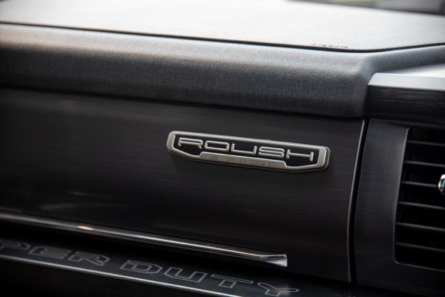 
                  
                    Close-up of a 2023 Roush Super Duty dashboard with a "ROUSH" emblem and part of an air vent visible, highlighting the Ford F-250’s performance suspension features.
                  
                