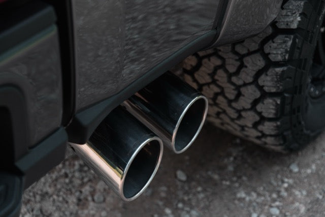 
                  
                    Close-up of dual chrome exhaust pipes on a 2023 Roush Super Duty next to a rugged tire, showcasing its performance suspension while parked on a gravel surface.
                  
                