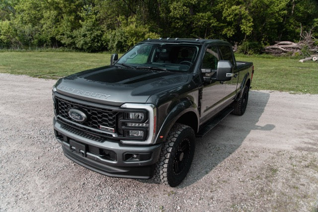 
                  
                    A dark gray 2023 Roush Super Duty Ford F-250 with performance suspension is parked on a gravel road near grass and trees.
                  
                