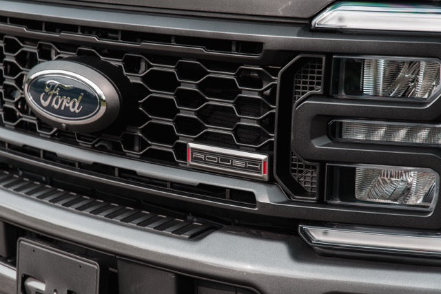 
                  
                    Close-up of the front grille on a 2023 Roush Super Duty Ford F-250, showcasing the distinctive "Roush" badge and part of the headlight—highlighting its bold style and performance suspension upgrades.
                  
                