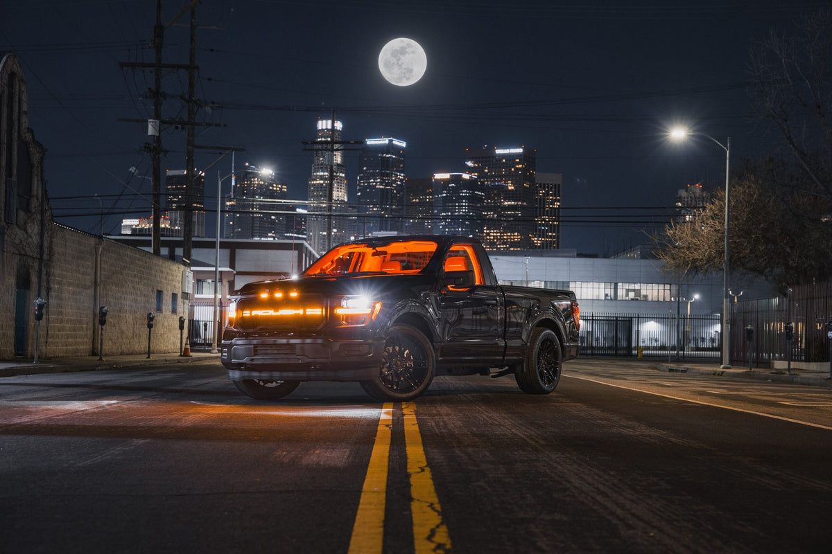 
                  
                    Black Roush Nitemare pickup truck parked on a city street at night with a full moon and skyline in the background.
                  
                