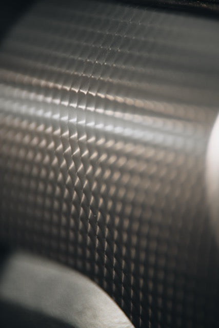 
                  
                    Close-up of a metallic surface with a repeating diamond pattern, illuminated by soft light creating shadows and texture variations—evoking the precision engineering of a TrakPak Mustang performance track car.
                  
                