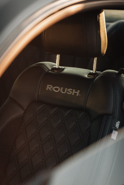 
                  
                    Black leather car seat with "ROUSH" embroidered on the headrest, shown through the open window of a high-performance Roush Mustang.
                  
                