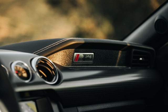 
                  
                    Close-up of a car dashboard showing air vents, textured trim, and a badge with a red "S" and "quattro" lettering—highlighting the refined details you’d expect in a high-end performance track car.
                  
                
