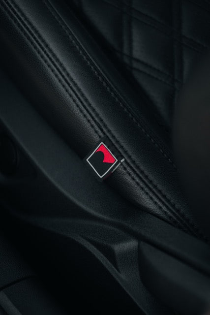 
                  
                    Close-up of a black leather car seat with a diamond-stitched pattern, featuring a small rectangular tag in red and black—an interior detail inspired by the TrakPak Mustang performance track car.
                  
                