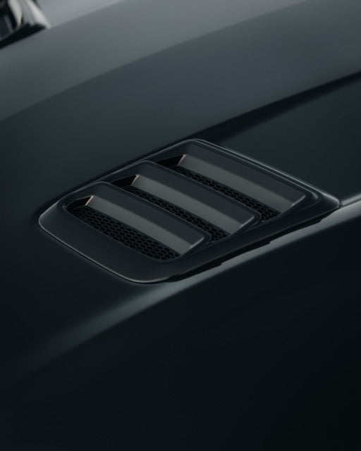 
                  
                    Close-up of a black Roush Mustang hood featuring a vent with three horizontal slats, highlighting its performance track car design.
                  
                