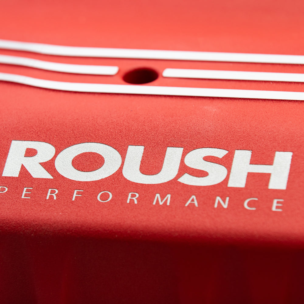 
                  
                    Close-up of a red surface with the white text "ROUSH Performance" and decorative white lines above it, hinting at the power of an 810-horsepower ROUSH Mustang Supercharger.
                  
                
