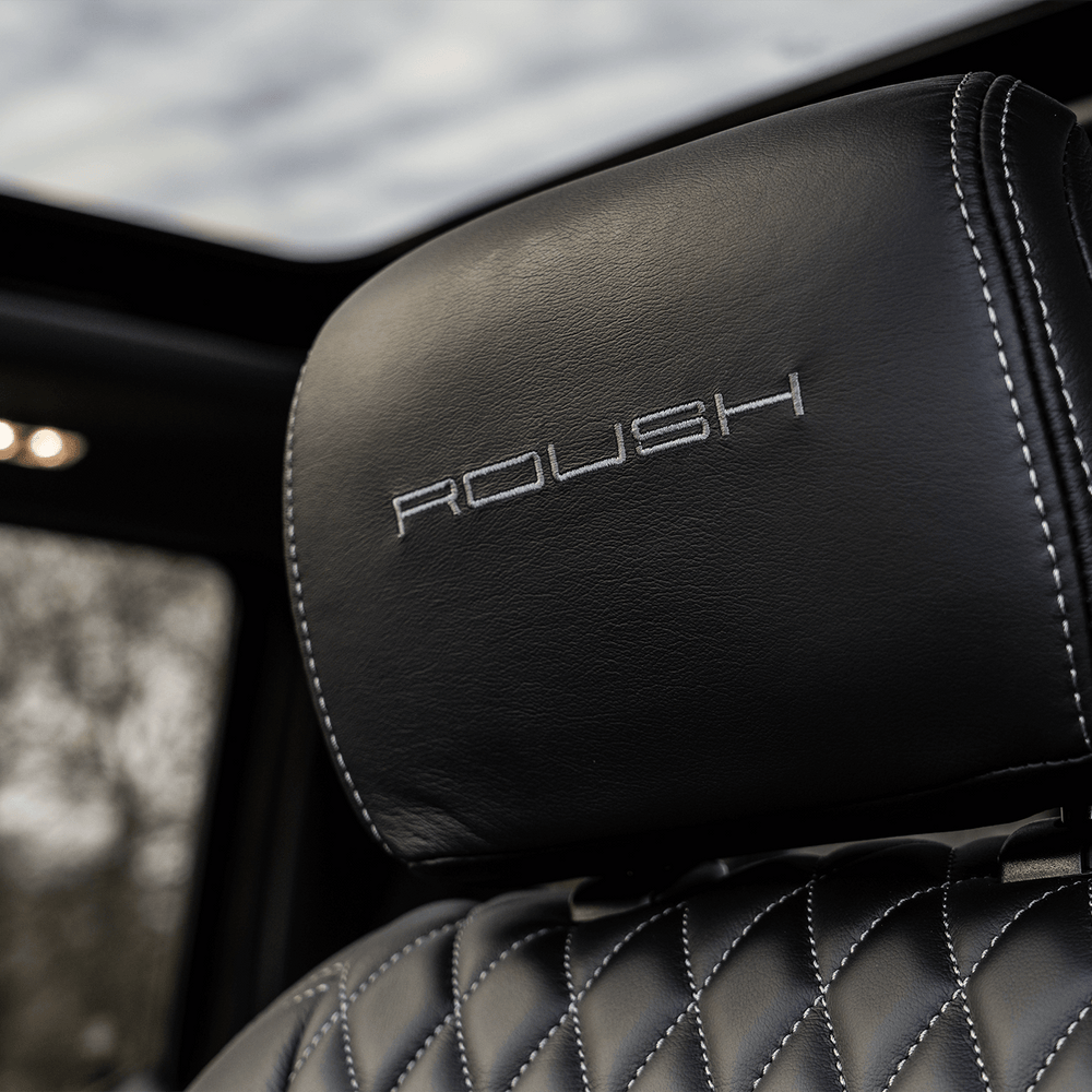 
                  
                    Close-up of a black leather car seat headrest with the word "ROUSH" embroidered in white stitching, with a view of the sunroof and cloudy sky visible above. The distinctive ROUSH High-Flow Front Grille of the 2022 ROUSH F-150 hints at the power and performance ready to be unleashed.
                  
                