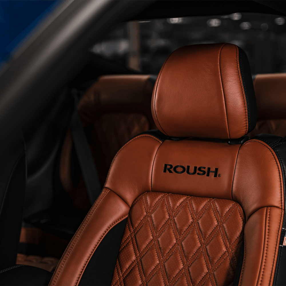 
                  
                    Close-up of a Roush Mustang's brown leather seat with "ROUSH" embroidered. The seat exudes performance, featuring a diamond-stitched pattern and an American flag tag on the side.
                  
                