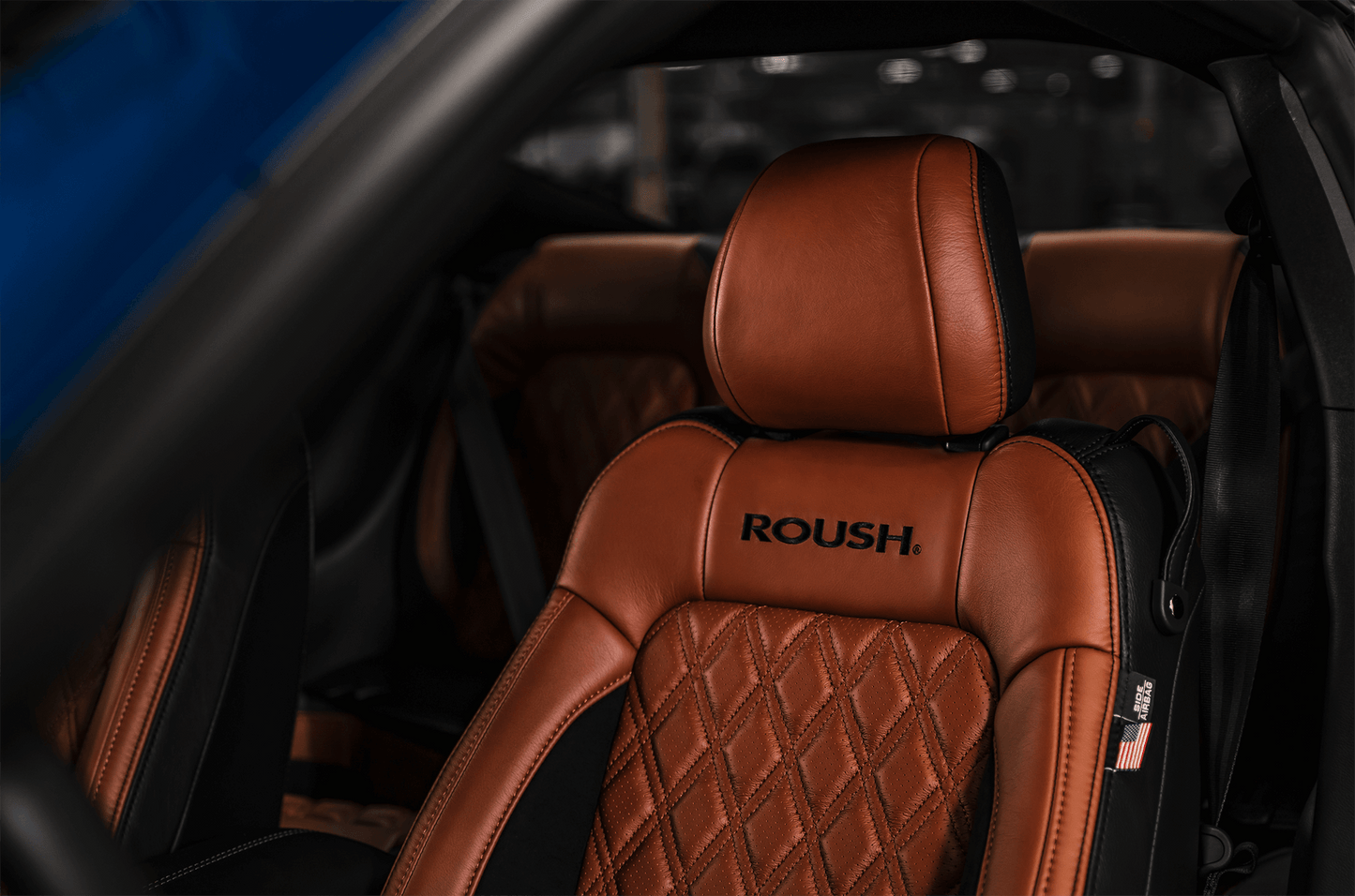 
                  
                    Close-up of a Roush Mustang's brown leather seat with "ROUSH" embroidered. The seat exudes performance, featuring a diamond-stitched pattern and an American flag tag on the side.
                  
                