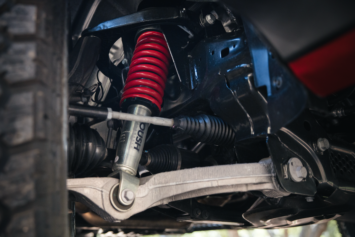 
                  
                    Close-up view of a Ram 1500 lift kit installed on the vehicle’s suspension system, featuring a red coil spring, shock absorber, and surrounding metal components.
                  
                