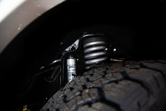 
                  
                    Close-up view of a Roush Super Duty vehicle's suspension system, featuring a coil spring and shock absorber above a tire, showcasing the robust performance suspension capabilities.
                  
                