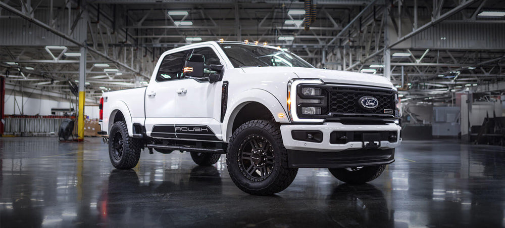 A White Ford Roush Super Duty pickup truck, equipped with a powerful turbodiesel V8 engine, is parked in a large industrial warehouse.