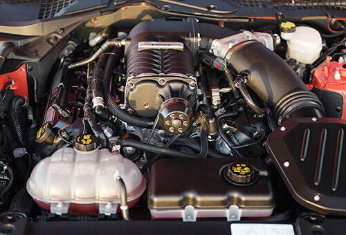 
                  
                    Close-up view of a car engine, featuring various components and hoses, with a focus on the central engine block of the EcoBoost Mustang.
                  
                